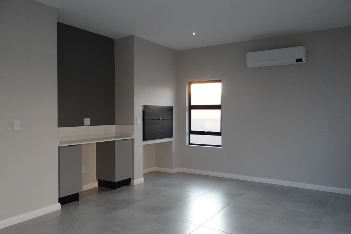 Modern living area featuring sleek tiled floors, a built-in braai, and an integrated air conditioning unit in a neutral, contemporary finish.