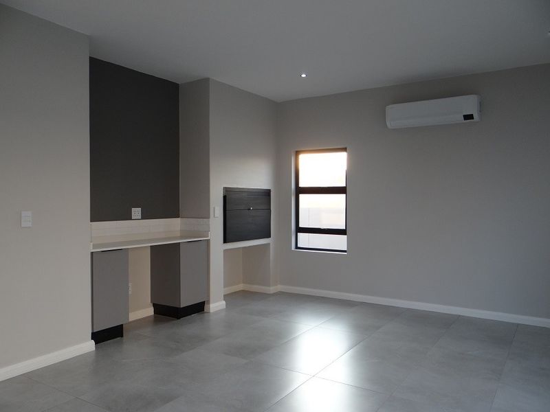 Modern living area featuring sleek tiled floors, a built-in braai, and an integrated air conditioning unit in a neutral, contemporary finish.