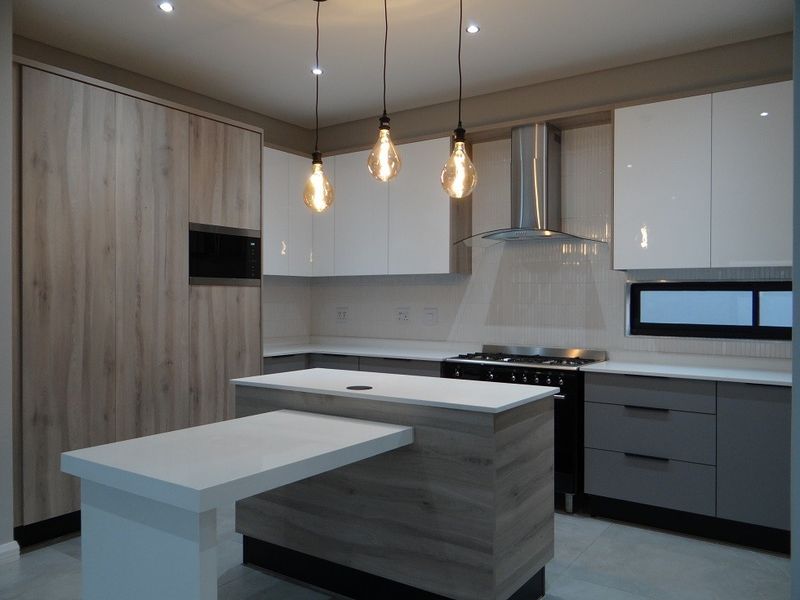 Modern kitchen featuring high-gloss white and wood-grain cabinetry, a central island with an integrated breakfast bar, stone countertops, and a professional-style gas stove.