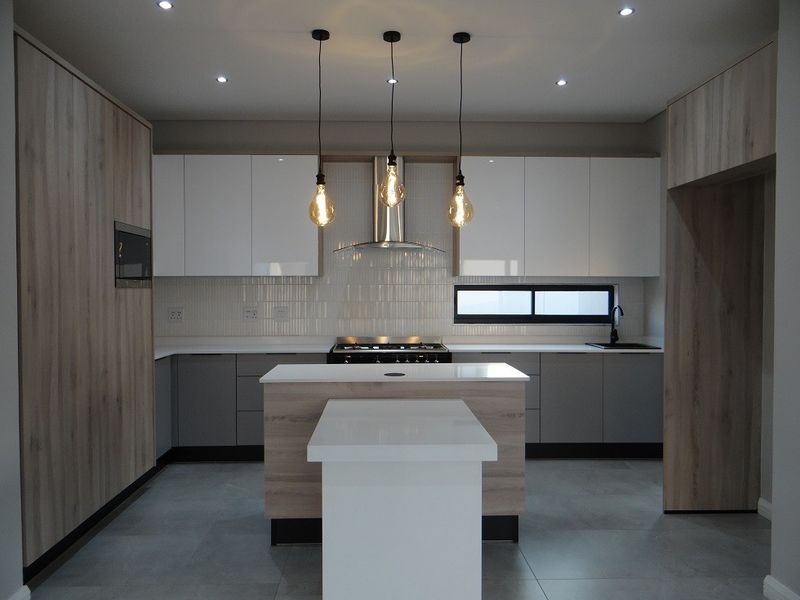 Modern kitchen featuring sleek two-tone cabinetry, a central island with stone countertops, integrated appliances, and contemporary recessed lighting.