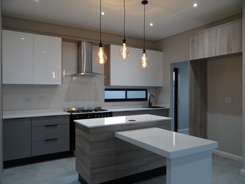 Modern kitchen featuring a central island with breakfast bar, high-gloss cabinetry, quartz countertops, built-in gas stove, and contemporary pendant lighting.