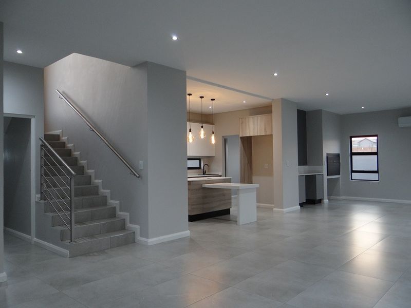 Spacious open-plan living area featuring modern tiled floors, a sleek kitchen island, built-in fireplace, and a contemporary staircase with stainless steel handrails.