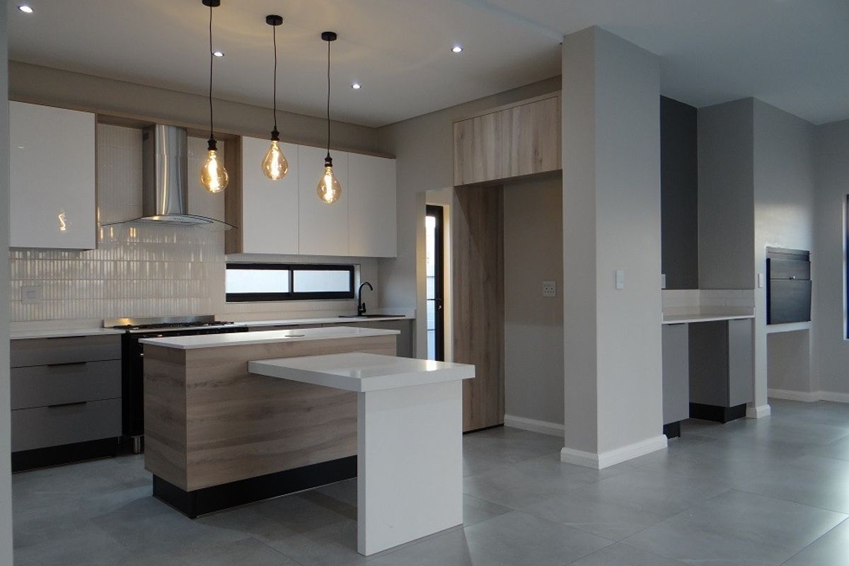 Modern, high-end kitchen featuring sleek cabinetry, a central island with breakfast bar, stone countertops, and integrated lighting in a contemporary open-plan layout.