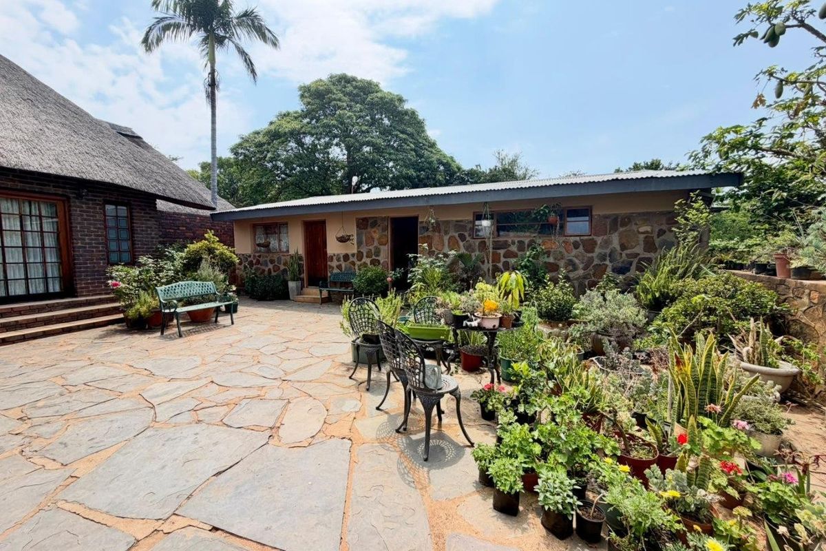 A charming rear courtyard featuring natural stone wall cladding, flagstone paving, and a mix of thatched and corrugated metal roofing structures.