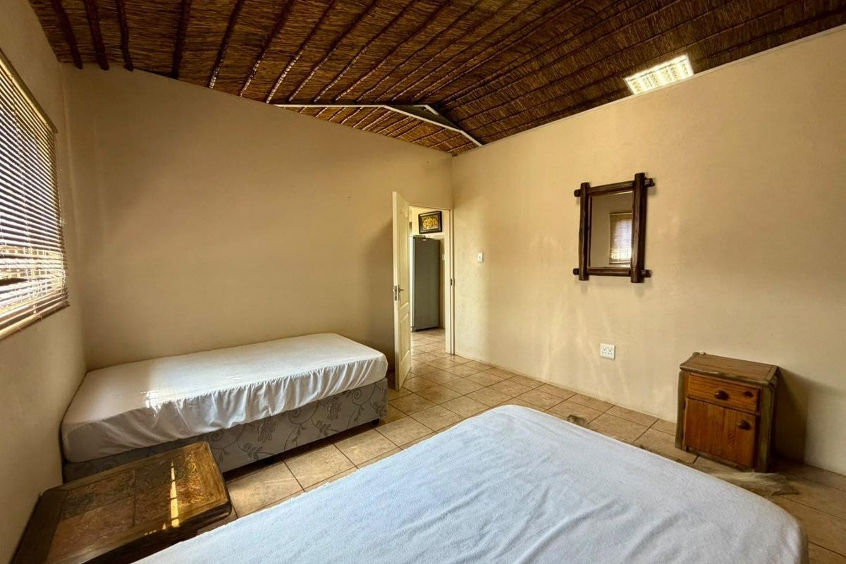 A bedroom featuring a traditional thatched ceiling, tiled flooring, and natural light through venetian blinds.