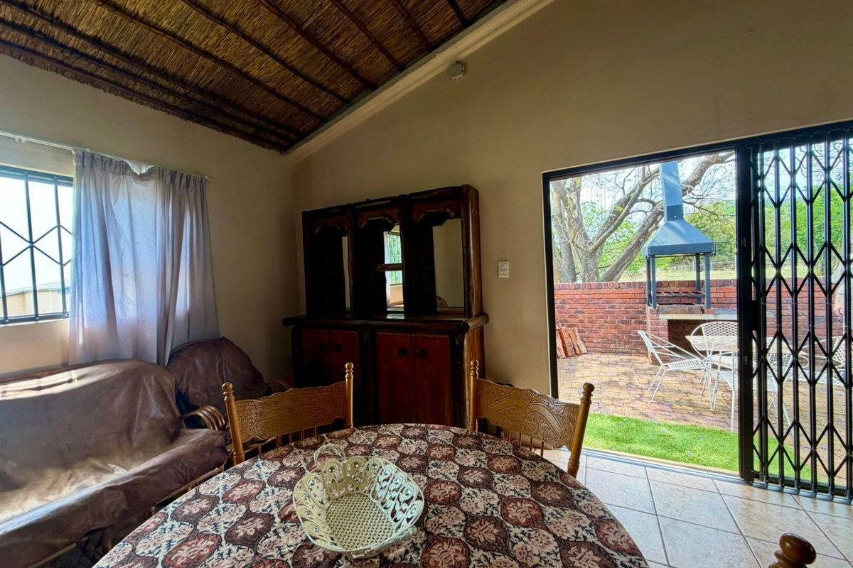 Living area featuring a traditional thatched ceiling and tiled floors, with direct access through sliding doors to a private patio with a built-in braai.