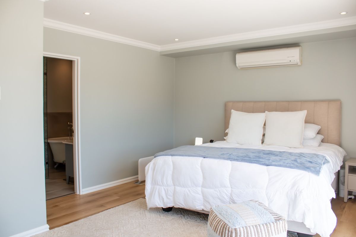 A well-maintained bedroom featuring light-toned walls, recessed ceiling lighting, crown molding, and a split-system air conditioning unit, with direct access to an en-suite bathroom.