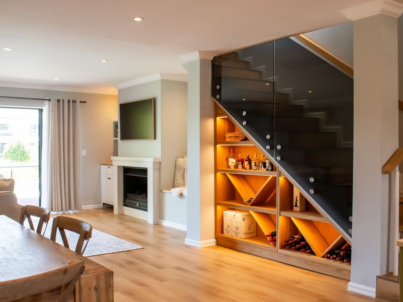 Modern open-plan living area featuring a built-in fireplace and custom under-stair wine storage with integrated lighting and a sleek glass balustrade.