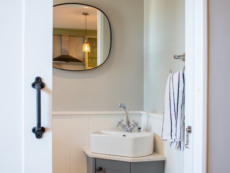 A compact, modern bathroom featuring a stylish vessel sink, stone countertop, vanity cabinet, and classic wainscoting detail.