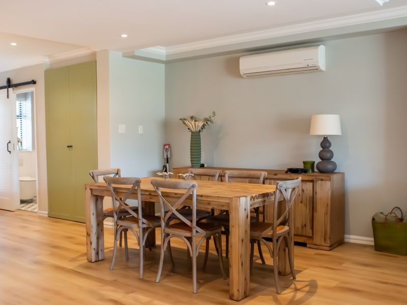A bright and well-maintained dining area featuring light timber flooring, recessed lighting, a split-system air conditioner, and a functional built-in storage cupboard.
