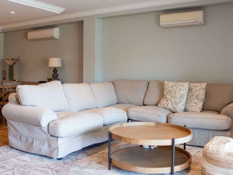 A comfortable living room featuring hardwood flooring, crown molding, recessed lighting, and dual split-system air conditioning units for climate control.
