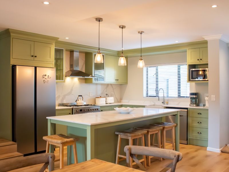 Modern kitchen featuring sage green cabinetry, a central island with quartz countertops, high-end integrated appliances, and stylish pendant lighting.