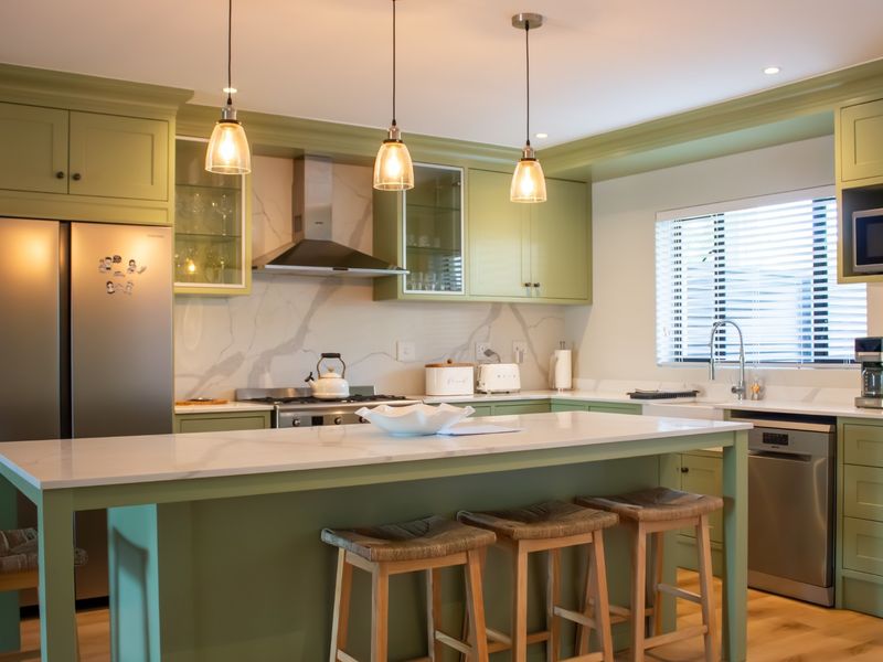 A modern, well-appointed kitchen featuring sage green shaker-style cabinetry, a central island with quartz countertops, and high-quality integrated appliances.