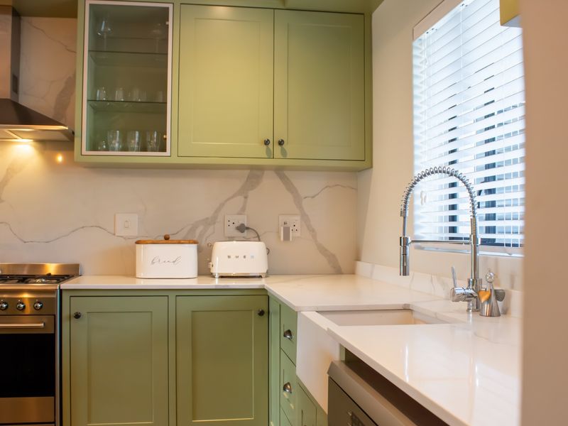 Modern kitchen featuring sage green cabinetry, marble-look quartz countertops, a farmhouse sink, and high-quality stainless steel appliances.