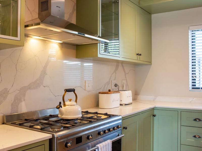 Modern kitchen featuring sage green shaker-style cabinetry, marble-look quartz countertops and splashback, and a high-quality gas stove with integrated extractor fan.