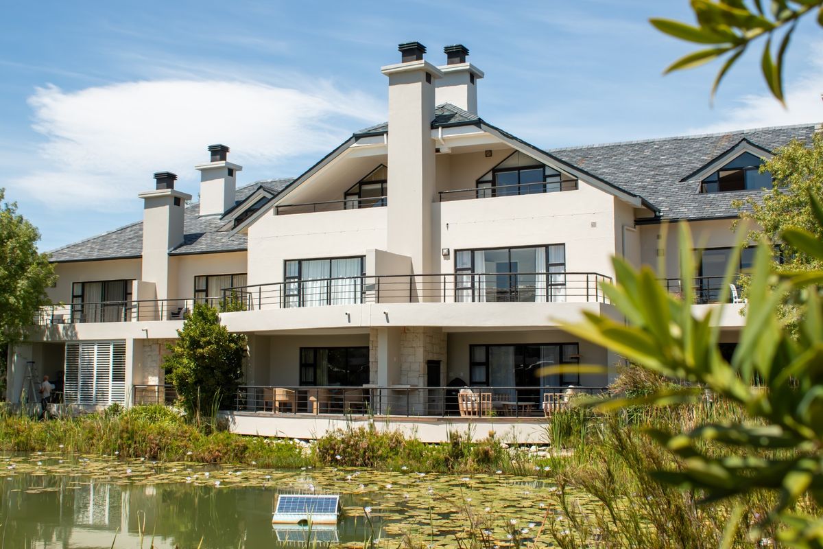 Rear elevation of a multi-story townhouse featuring multiple balconies, stone accents, and a slate roof, overlooking a landscaped pond.