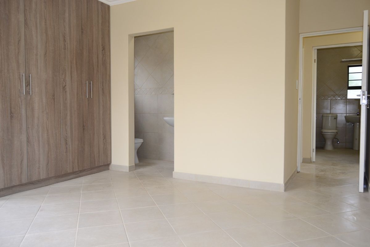 Spacious bedroom featuring neutral tiled flooring, ample built-in cupboard storage, and direct access to an en-suite bathroom.