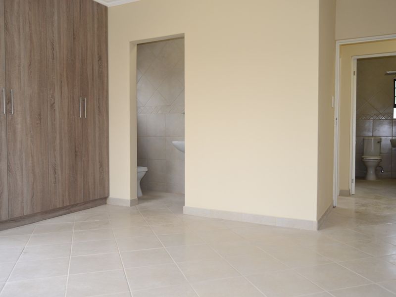 Spacious bedroom featuring neutral tiled flooring, ample built-in cupboard storage, and direct access to an en-suite bathroom.