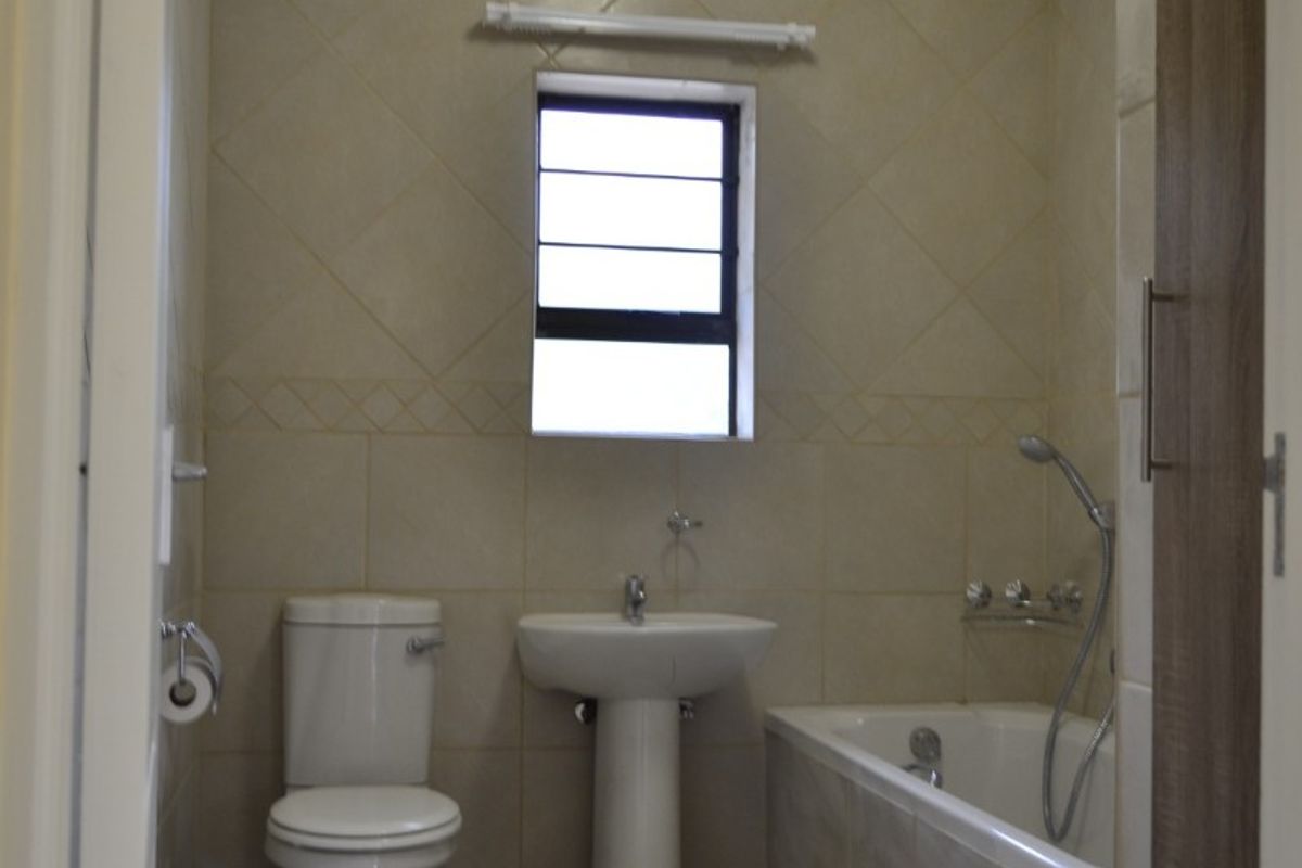 A functional bathroom featuring a pedestal basin, toilet, and bathtub with a handheld shower mixer, finished with neutral wall and floor tiles.
