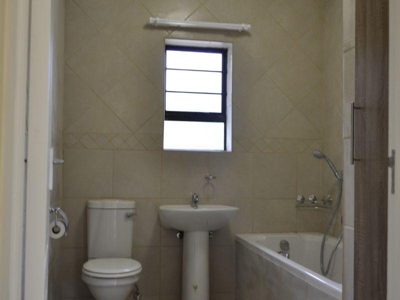 A functional bathroom featuring a pedestal basin, toilet, and bathtub with a handheld shower mixer, finished with neutral wall and floor tiles.