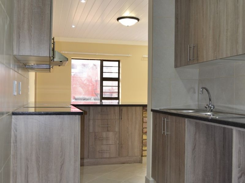Modern kitchen featuring wood-look cabinetry, granite countertops, stainless steel sink, and a clean, neutral tiled finish throughout.