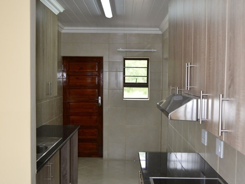 A clean, modern kitchen featuring wood-finish cabinetry, granite countertops, built-in oven and hob, and tiled finishes throughout.