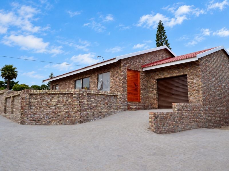 A modern face brick house featuring a tiled roof, a paved driveway, and an integrated roll-up garage door with a secure brick boundary wall.