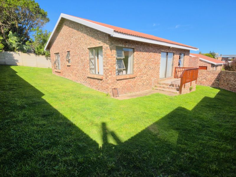 Rear view of a face brick house featuring a small wooden deck, sliding glass doors, and a private enclosed garden with boundary walls.
