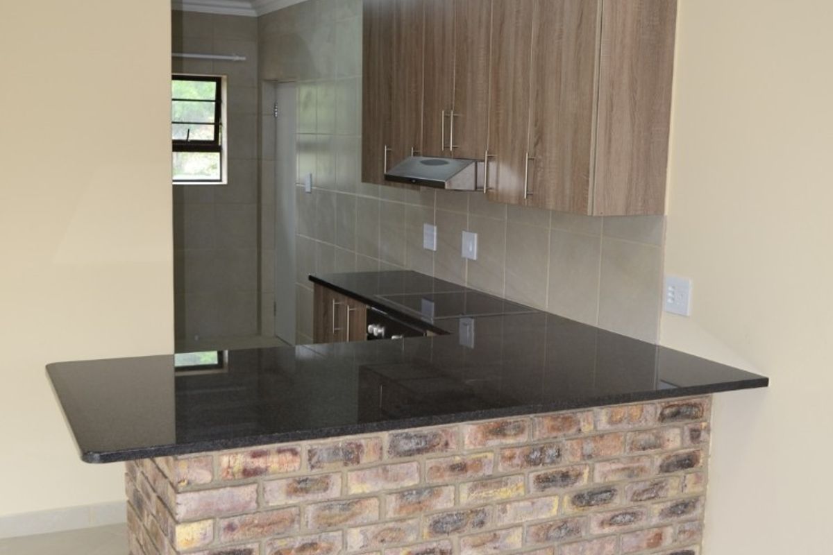 Modern kitchen featuring an exposed brick breakfast bar, granite countertops, built-in cabinetry, and a tiled backsplash in a clean, open-plan layout.