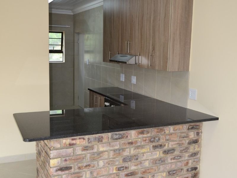 Modern kitchen featuring an exposed brick breakfast bar, granite countertops, built-in cabinetry, and a tiled backsplash in a clean, open-plan layout.