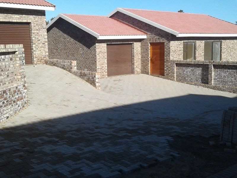 Front exterior view of a face brick house featuring a paved driveway, multiple roller shutter garage doors, and a secure boundary wall.