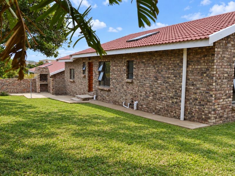 Rear view of a face brick house featuring a tiled roof, built-in braai area, concrete patio, and a well-maintained lawn.