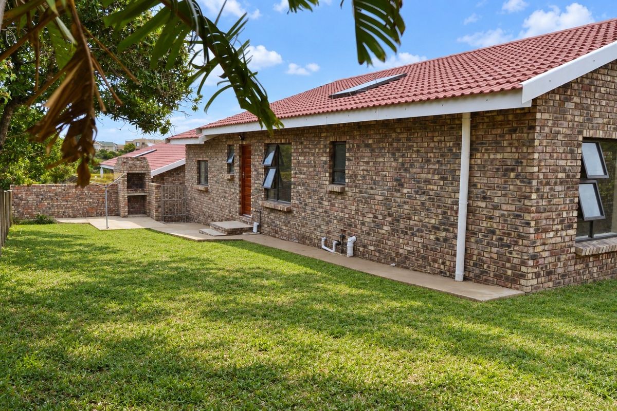 Rear view of a face brick house featuring a tiled roof, built-in braai area, concrete patio, and a well-maintained lawn.