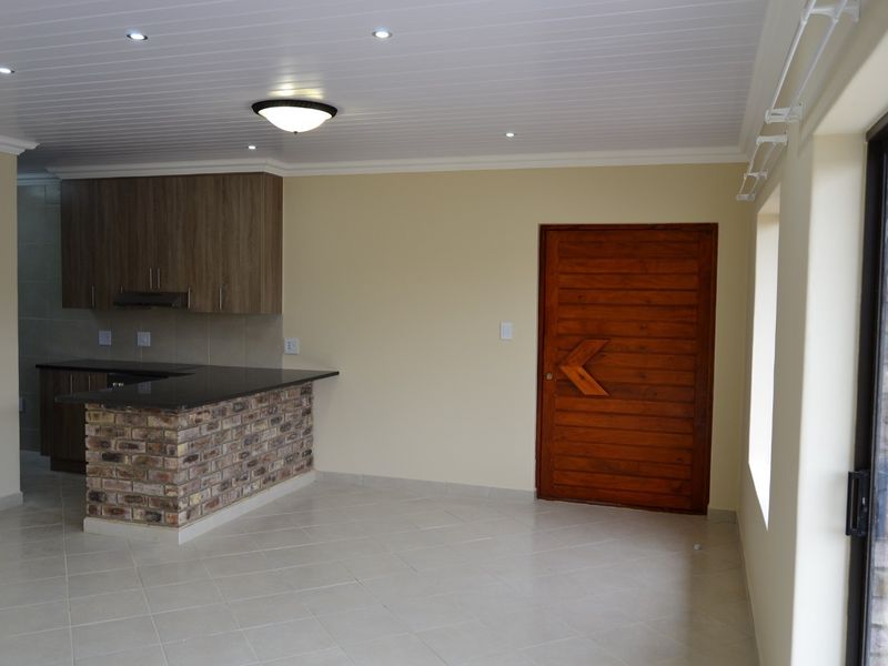 Open-plan living area featuring a kitchen with granite countertops, exposed brick breakfast bar, tiled flooring, and direct access to the exterior via a sliding door.