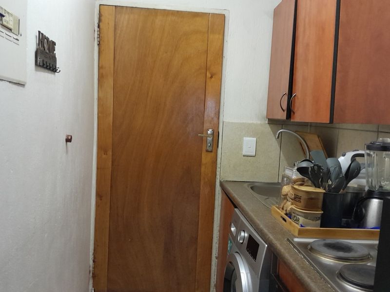 A compact kitchen area featuring built-in cabinetry, a sink, and an integrated electric hob, showing signs of age and wear.