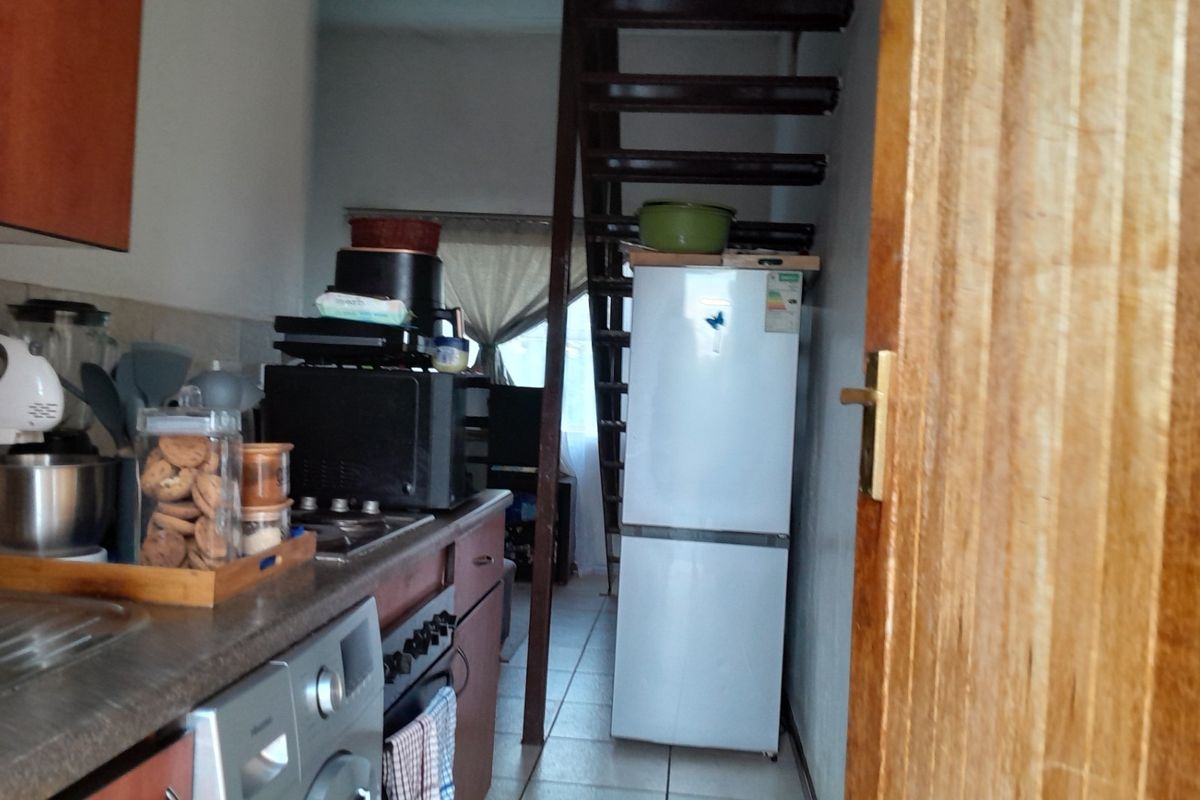 A compact kitchen area featuring built-in cabinetry, a hob, and an oven, with an adjacent staircase leading to another level.