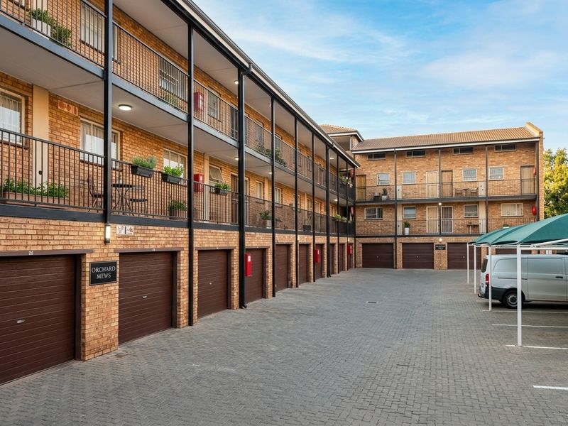 Exterior view of a multi-story apartment complex featuring brick facade, individual garage units, and balcony access for upper-level residences.