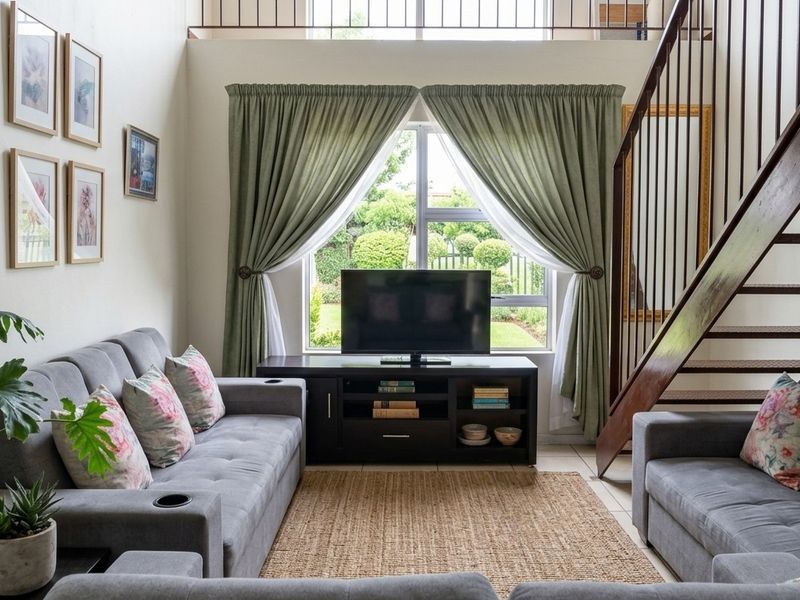 A bright living room featuring a staircase leading to a mezzanine level, large window with garden views, and neutral tiled flooring.