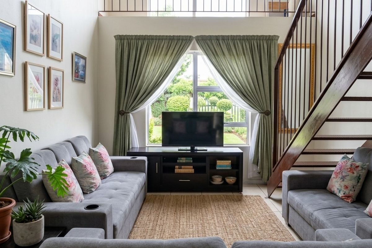 A bright living room featuring a staircase leading to a mezzanine level, large window with garden views, and neutral tiled flooring.