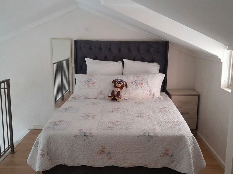 A cozy loft-style bedroom featuring sloped ceilings, laminate flooring, and a built-in cupboard, overlooking the lower level via a metal balustrade.