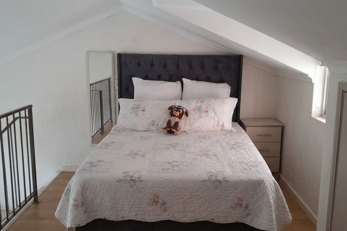 A cozy loft-style bedroom featuring sloped ceilings, laminate flooring, and a built-in cupboard, overlooking the lower level via a metal balustrade.