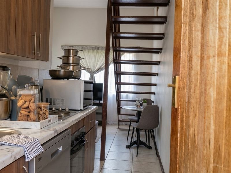 An open-plan kitchen area featuring modern cabinetry, marble-look countertops, and a staircase leading to an upper level, with tiled flooring throughout.