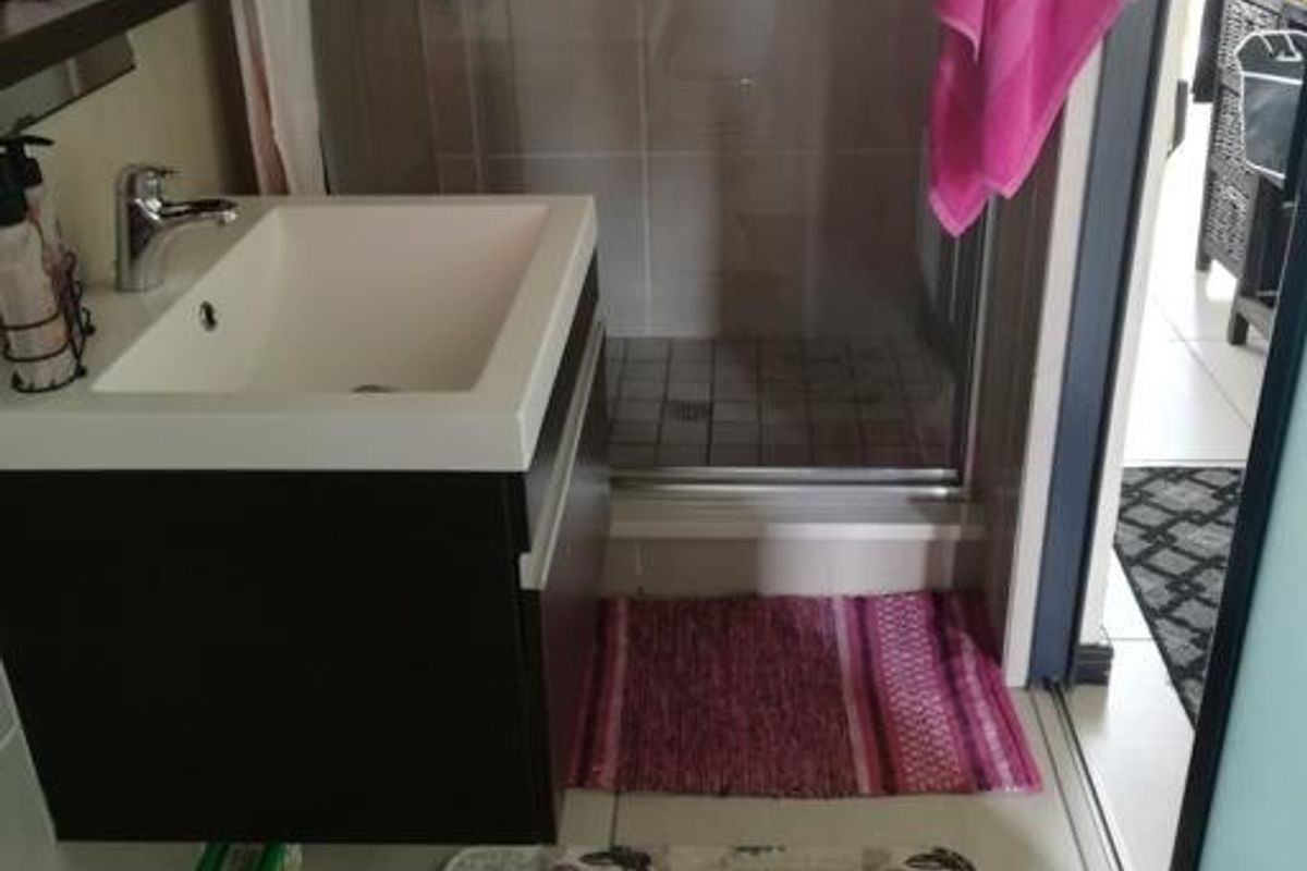 A compact modern bathroom featuring a wall-mounted vanity with basin, mixer tap, and a glass-enclosed shower with tiled finishes.
