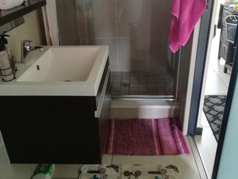 A compact modern bathroom featuring a wall-mounted vanity with basin, mixer tap, and a glass-enclosed shower with tiled finishes.
