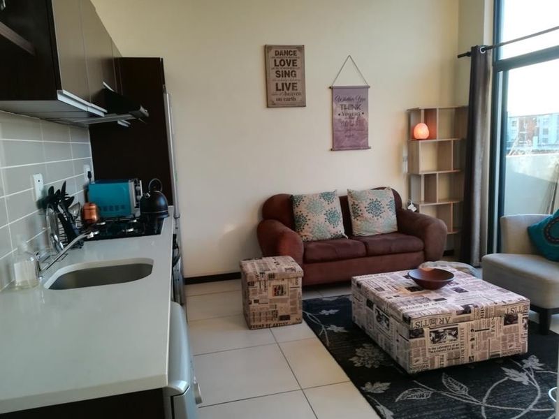 Open-plan living area featuring a modern kitchen with built-in cabinetry, gas hob, and tiled flooring, leading to a bright space with large glass doors.