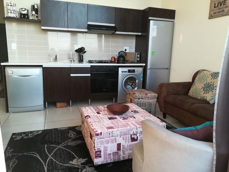 An open-plan living area featuring a compact kitchen with dark cabinetry, tiled backsplash, built-in oven, gas hob, and integrated appliances.