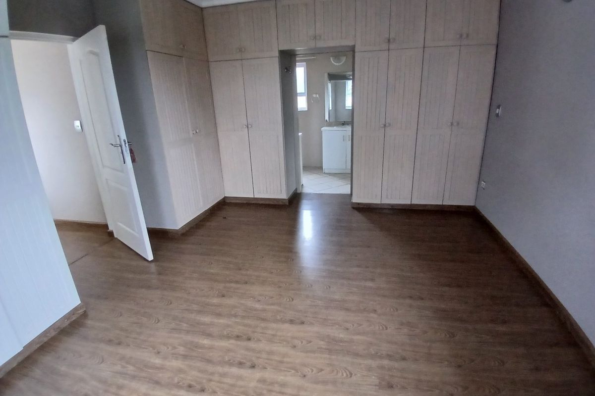 Spacious bedroom featuring extensive built-in cupboards, laminate flooring, and direct access to an en-suite bathroom.