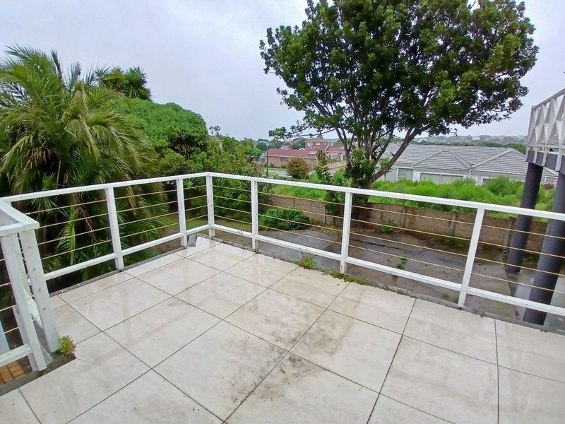 An elevated balcony featuring tiled flooring and a white metal railing with cable balustrade, offering an open outdoor space with neighbourhood views.