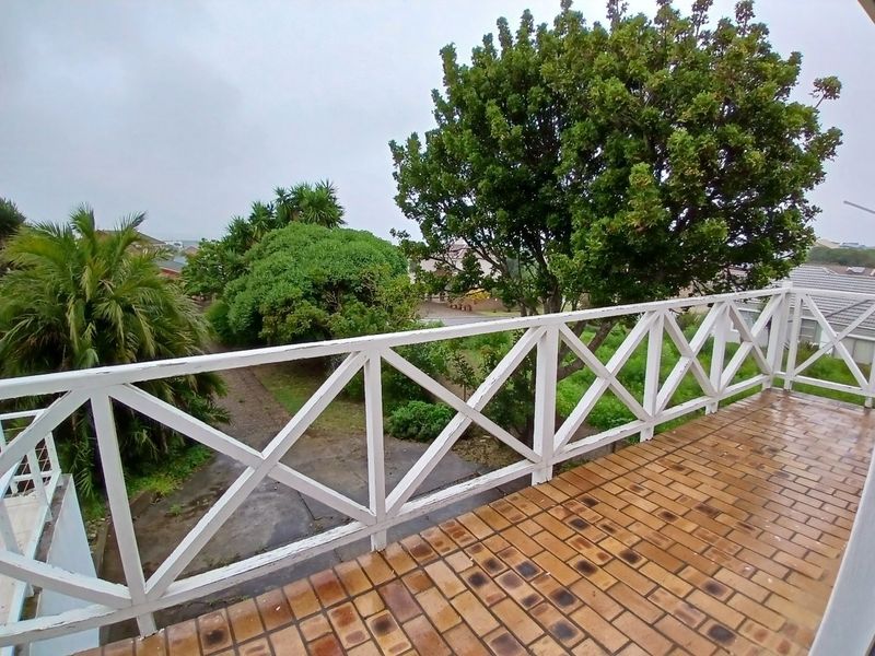 An elevated balcony featuring brick paving and a white wooden balustrade, overlooking the surrounding garden and neighborhood.