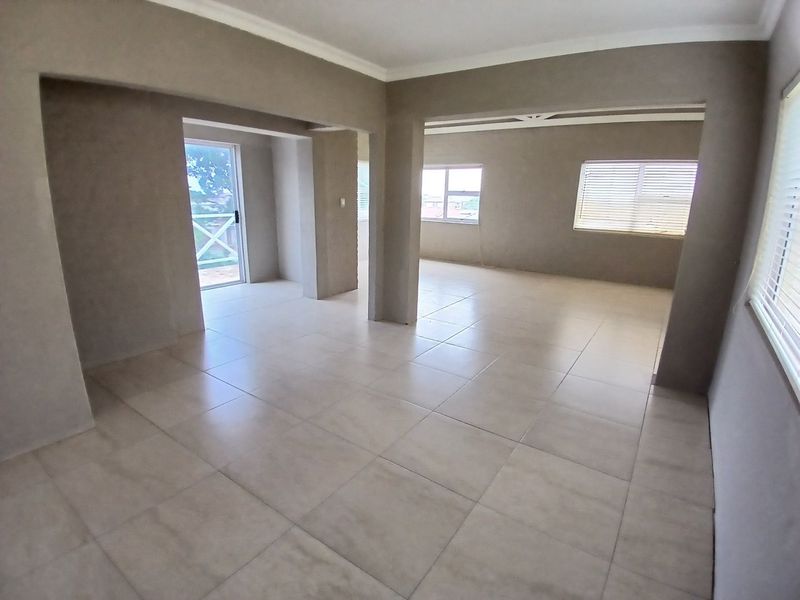 Spacious open-plan living area featuring neutral tiled flooring, large windows with blinds, and direct access to an outdoor space.